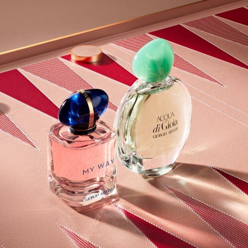 Armani Mother’s Day duo of "My Way" and "Acqua di Gioia" perfumes on a pink backgammon board with red triangular accents and elegant gaming pieces.