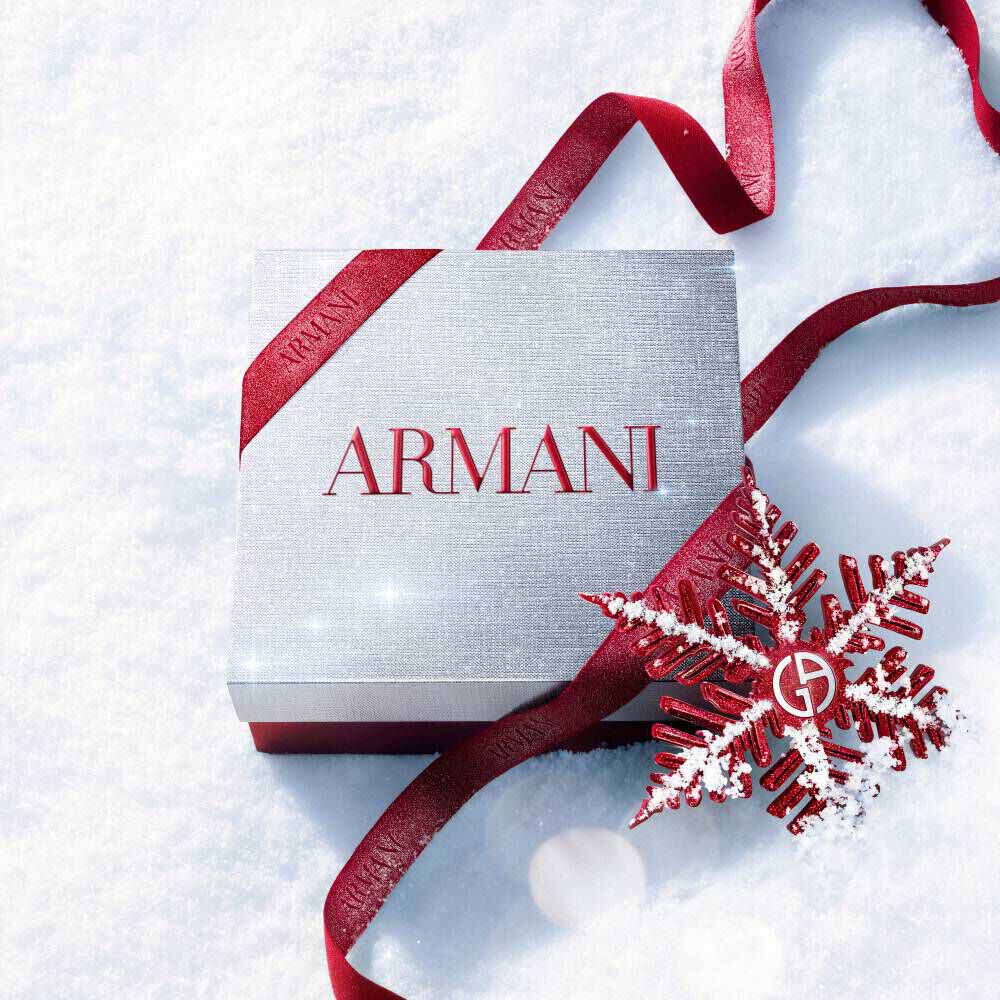 Armani beauty Holiday 2026 white gift box tied with a red ribbon and snowflake decoration on a snowy surface