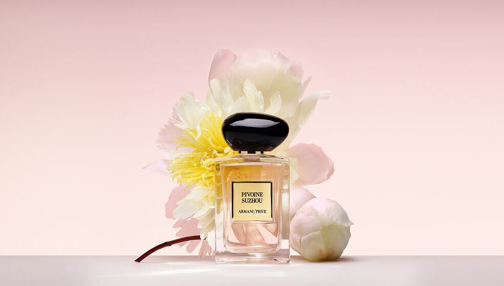 Bottle of Armani/Prive Pivoine Suzhou fragrance agaisnt a light pink background and floral ingredients.
