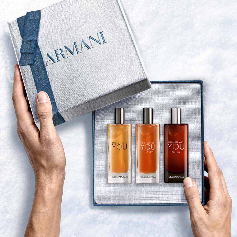 Emporio Armani Stronger With You Eau de Toilette 15ml, Stronger With You Intensely 15ml and Stronger With You Parfum 15ml — hands unveiling the three-piece fragrance gift set from within the open Armani gift box, an intimate unboxing moment.