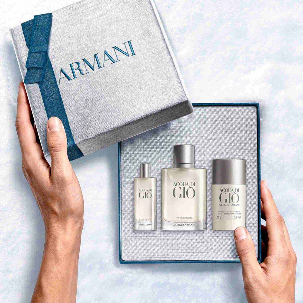 Giorgio Armani Acqua di Gio Eau de Toilette 100ml gift set — hands unveiling the signature bottle,and Deodorant Stick 75g from within the open Armani gift box, an intimate unboxing moment.