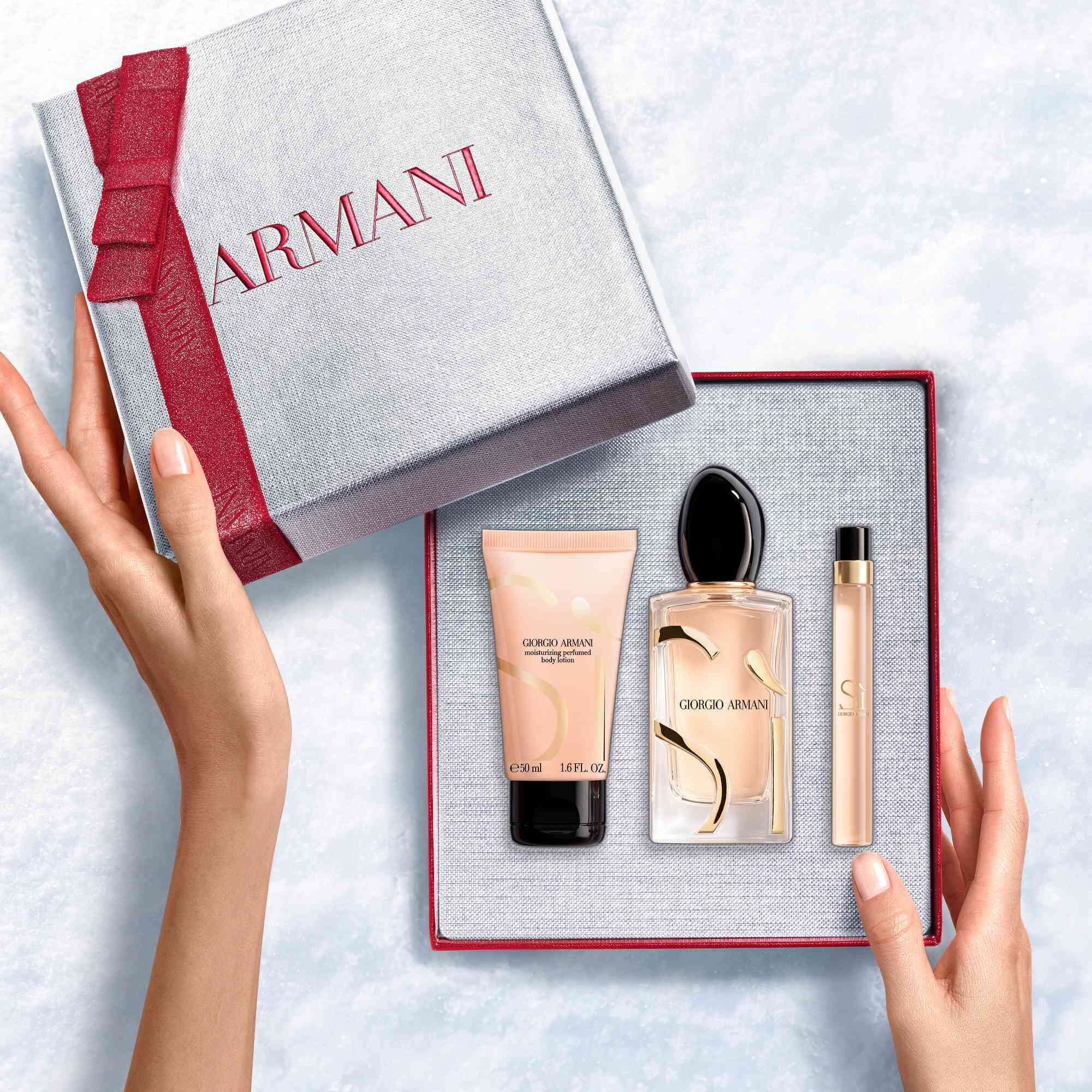 Hands unveiling a red-ribboned white Armani gift box with Si Eau de Parfum 100ml, Travel size10ml and 50ml perfumed body lotion — a refined women's floral fragrance gift set.
