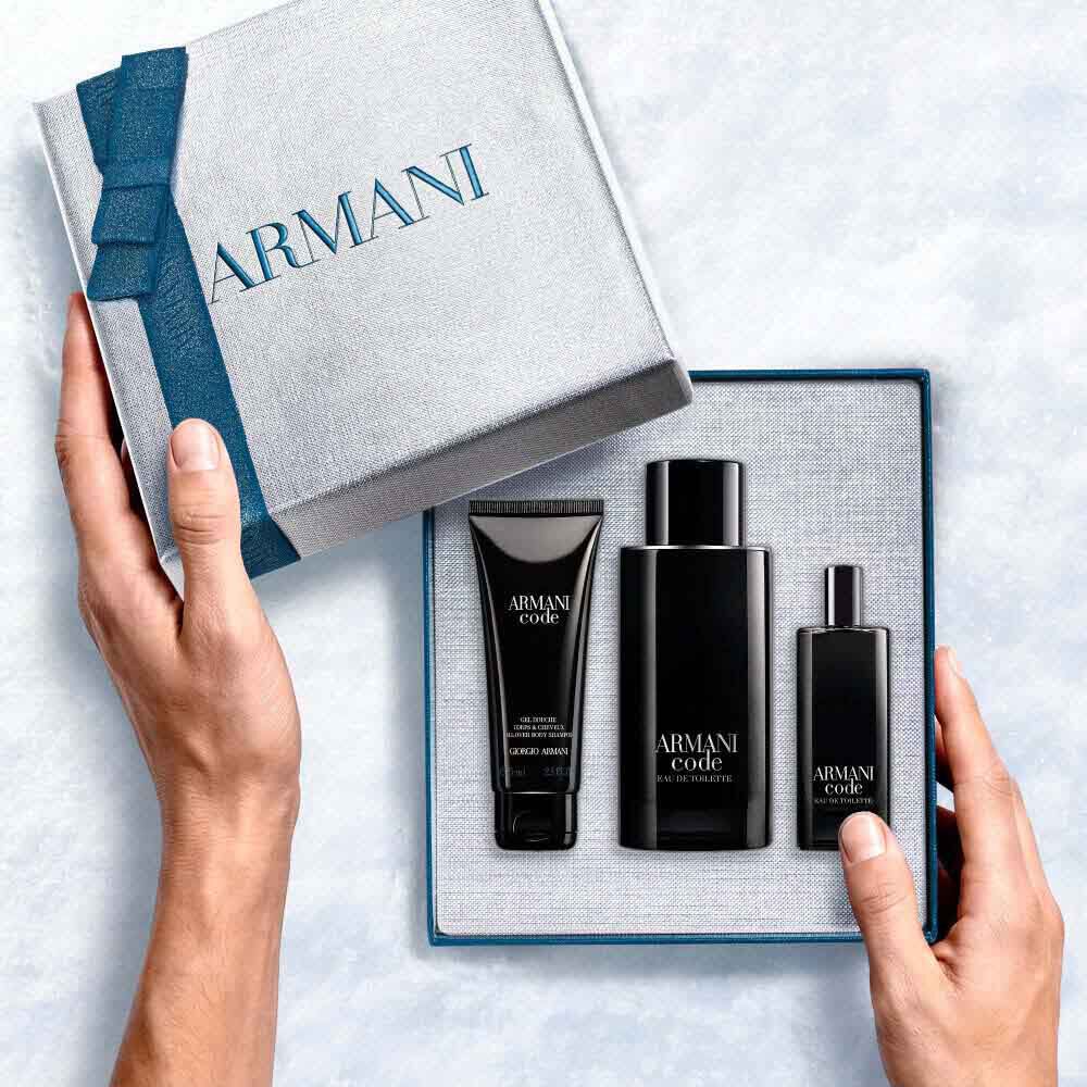 Hands opening a teal-ribboned Armani gift box revealing Armani Code Eau de Toilette 125ml, 15ml and All-Over Body Shampoo 75g — men's fragrance gift set.