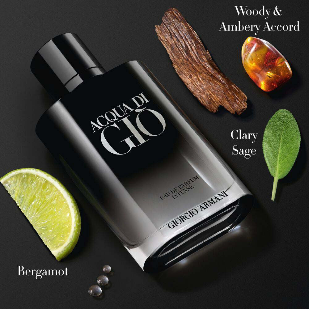 Acqua di Gio Eau de Parfum Intense by Giorgio Armani, black bottle flat-lay with bergamot, clary sage leaf, cedarwood, and amber resin on a dark background — men's woody ambery fragrance.