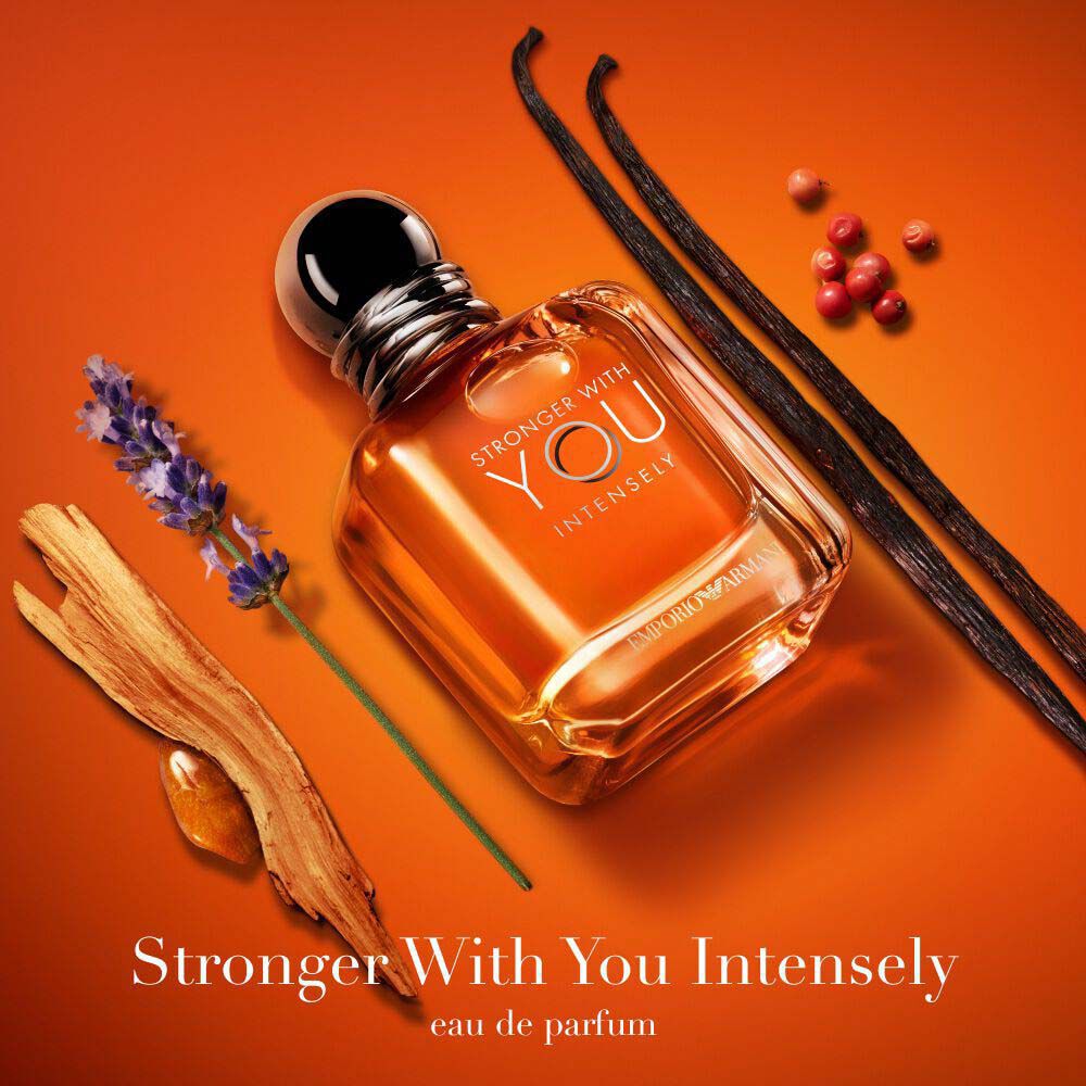 Emporio Armani Stronger With You Intensely Eau de Parfum — signature amber bottle surrounded by key olfactive ingredients: lavender, pink pepper, vanilla, and amber wood on a warm orange background.