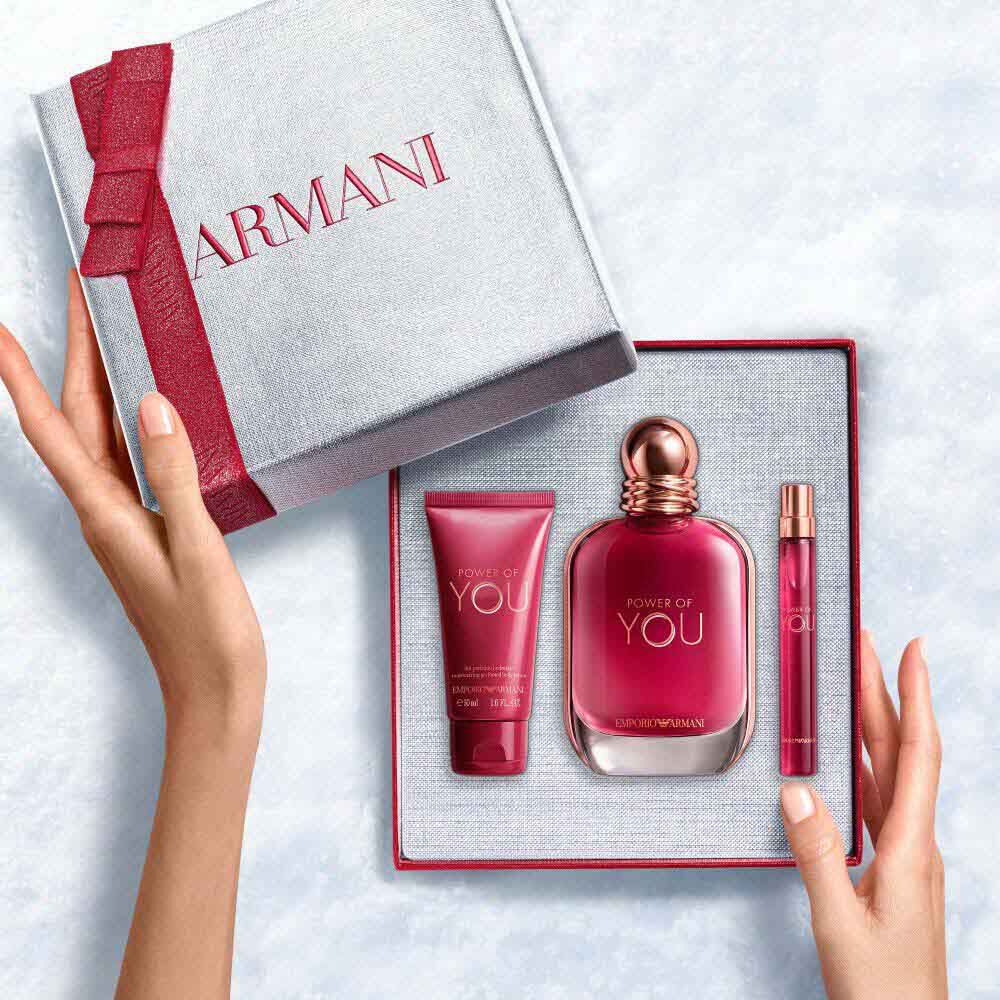 Hands unveiling a red-ribboned white Armani gift box with Power of You Eau de Parfum 50ml in a sleek ruby bottle, Power of You Eau de Parfum 10ml  and 50ml perfumed body lotion — a bold, feminine fragrance gift set for women.