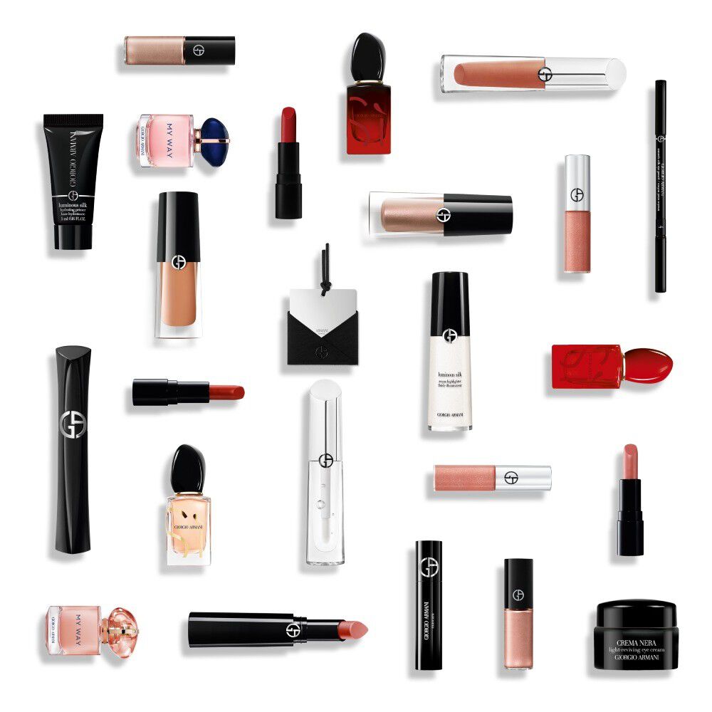 A flat lay arrangement of various Giorgio Armani beauty products, including black mascara tubes, red and nude lipsticks, liquid foundations, a pink perfume bottle, compacts	