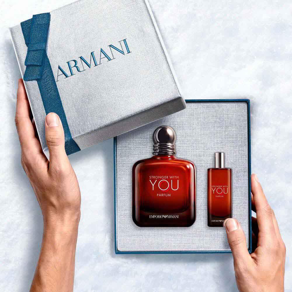 Two hands lifting the lid of the Armani gift box to reveal the Emporio Armani Stronger With You  Parfum gift set — overhead unboxing moment on a pale surface.