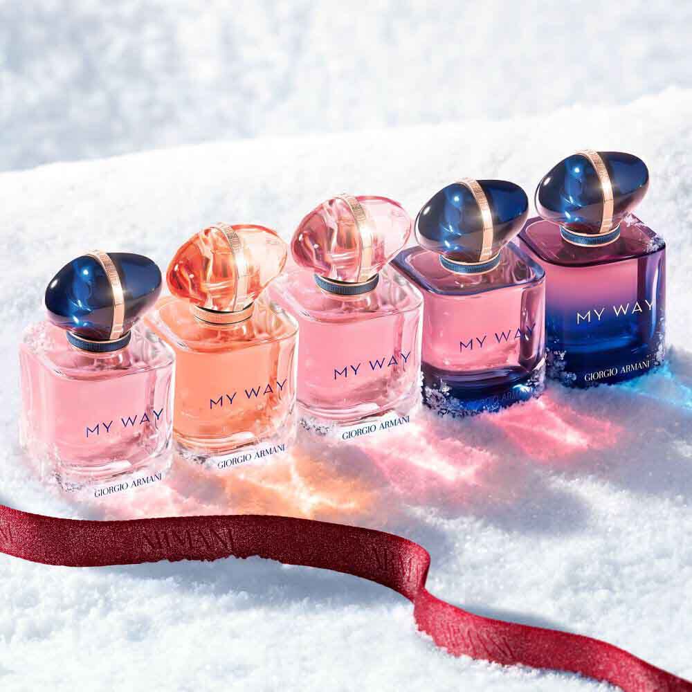 My Way fragrance collection — Eau de Parfum, Intense and Le Parfum — in pink and violet bottles lined up on a snowy surface with a ruby ribbon —