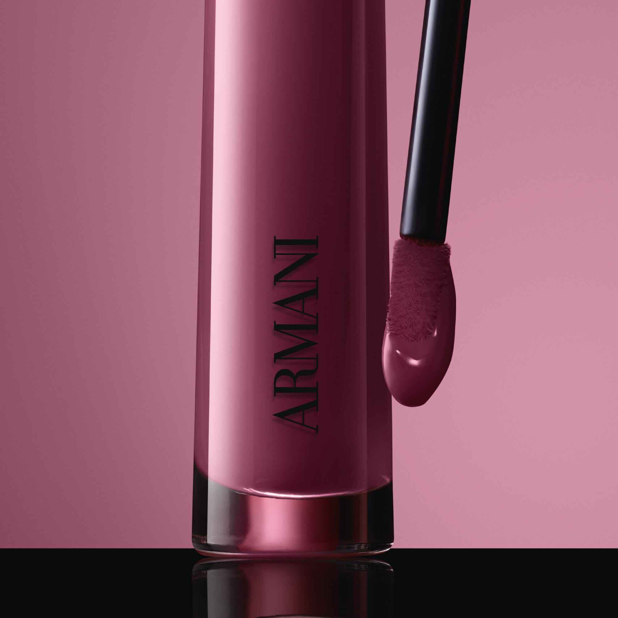 Close-up of the black ARMANI LIP MAESTRO cap with gold logo and its applicator coated in shade 520 Dusty Rose against a pink background.