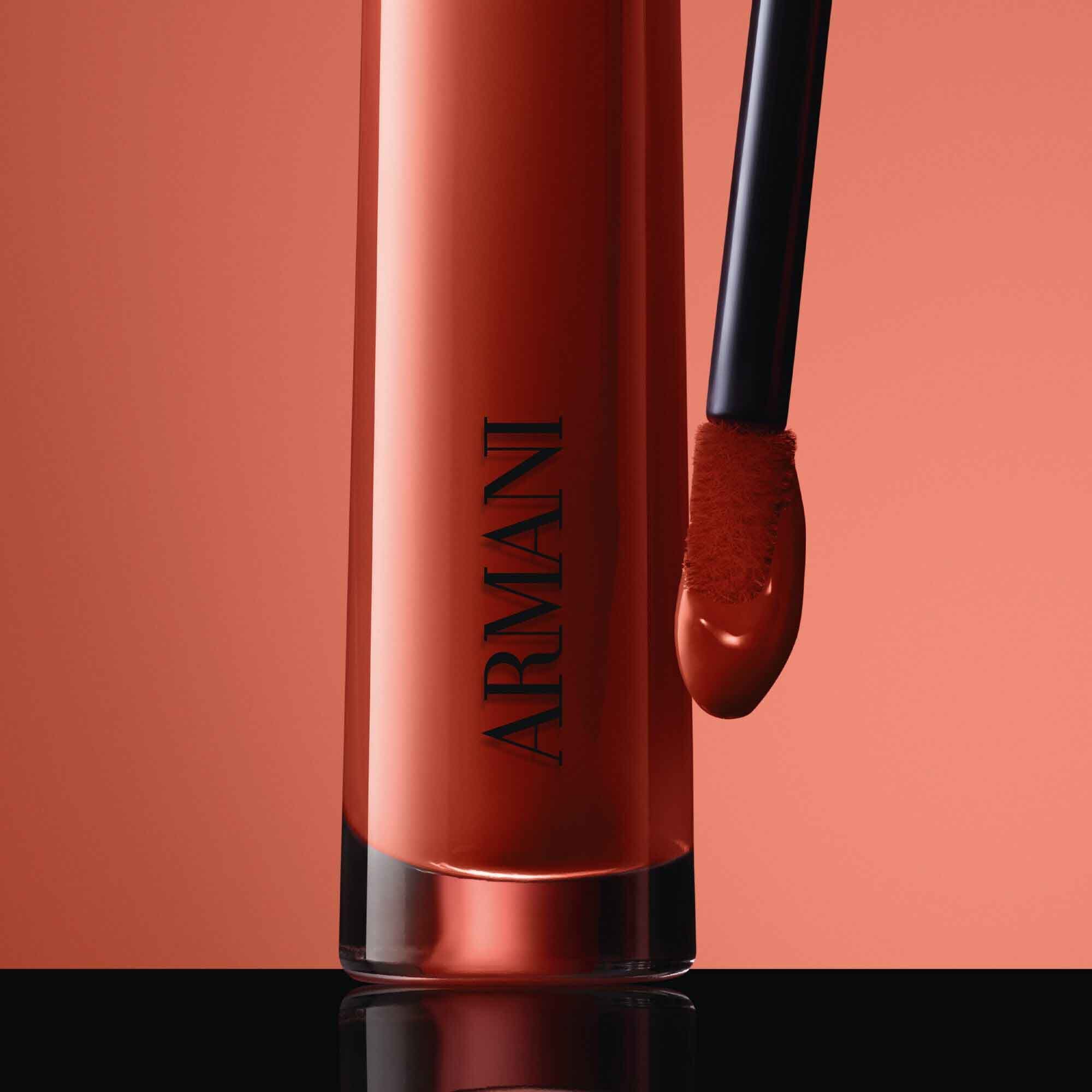 Close-up of the black ARMANI LIP MAESTRO cap with gold logo and its applicator coated in shade 520 Dusty Rose against a pink background.
