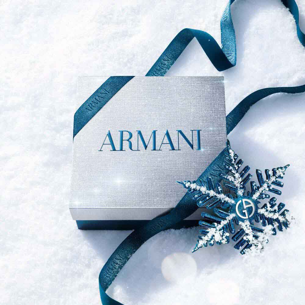 Emporio Armani Stronger With You Parfum gift box wrapped in teal satin ribbon with a snowflake decoration, placed on a white winter surface — holiday gifting presentation.