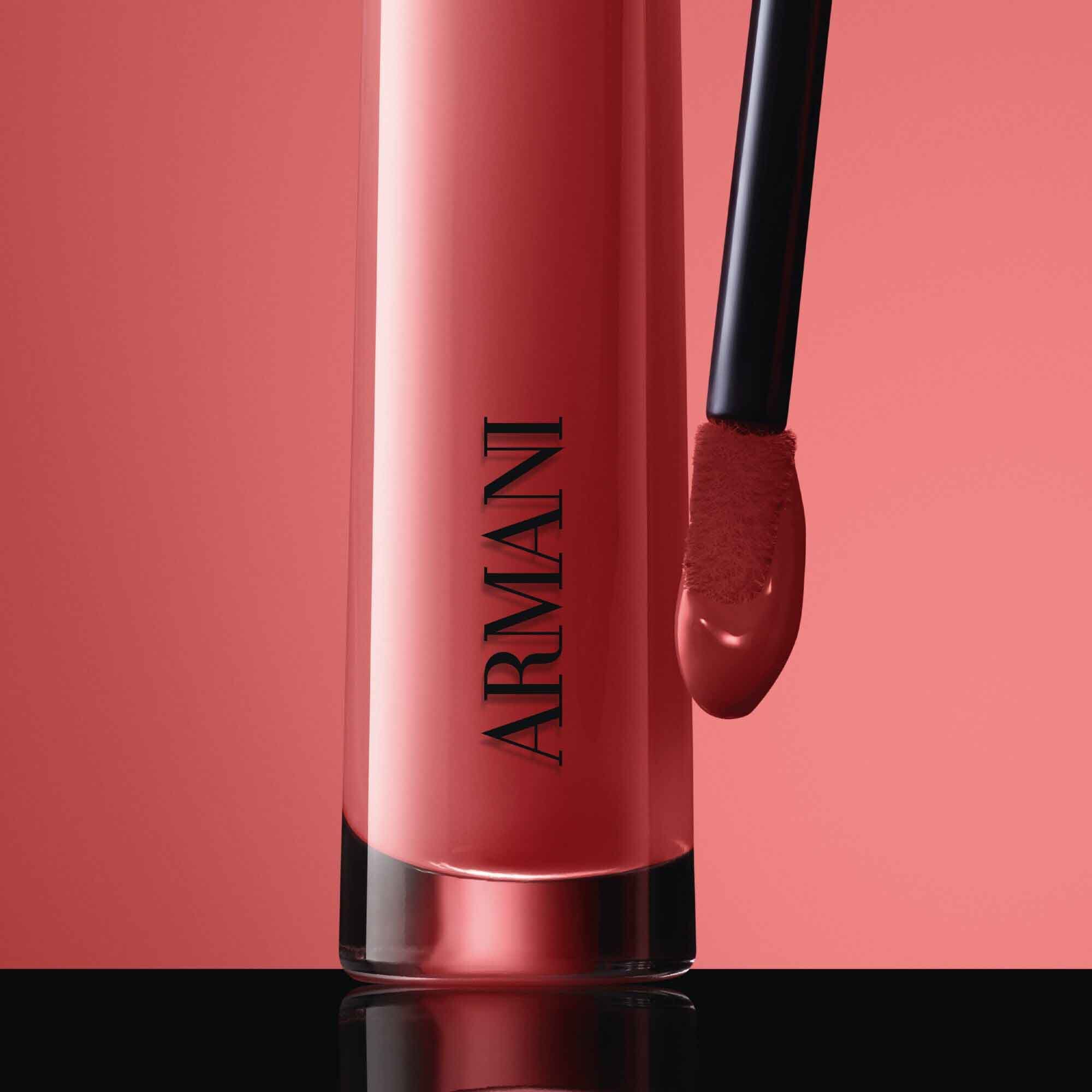Close-up of the black ARMANI LIP MAESTRO cap with gold logo and its applicator coated in shade 520 Dusty Rose against a pink background.
