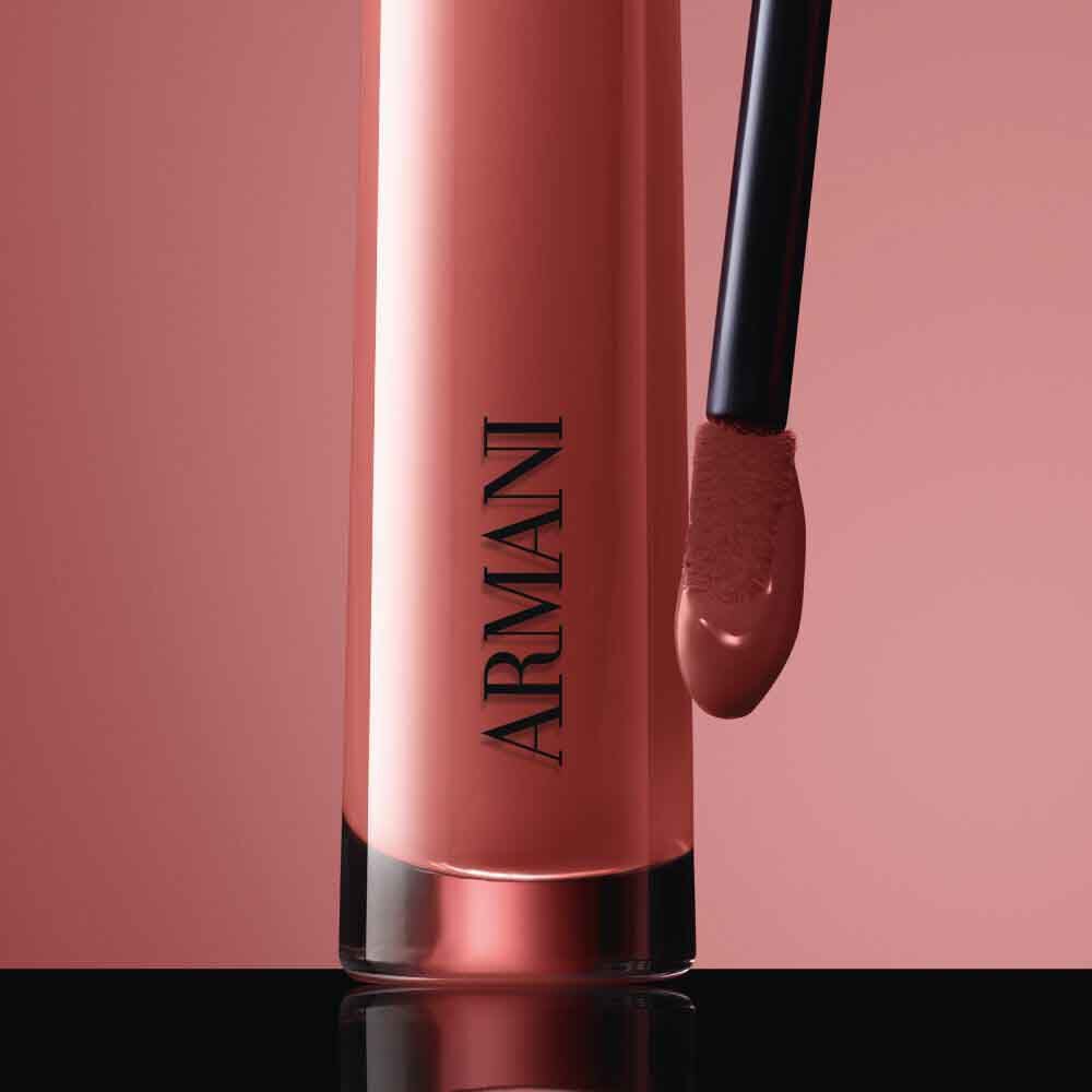 Close-up of the black ARMANI LIP MAESTRO cap with gold logo and its applicator coated in shade 520 Dusty Rose against a pink background.