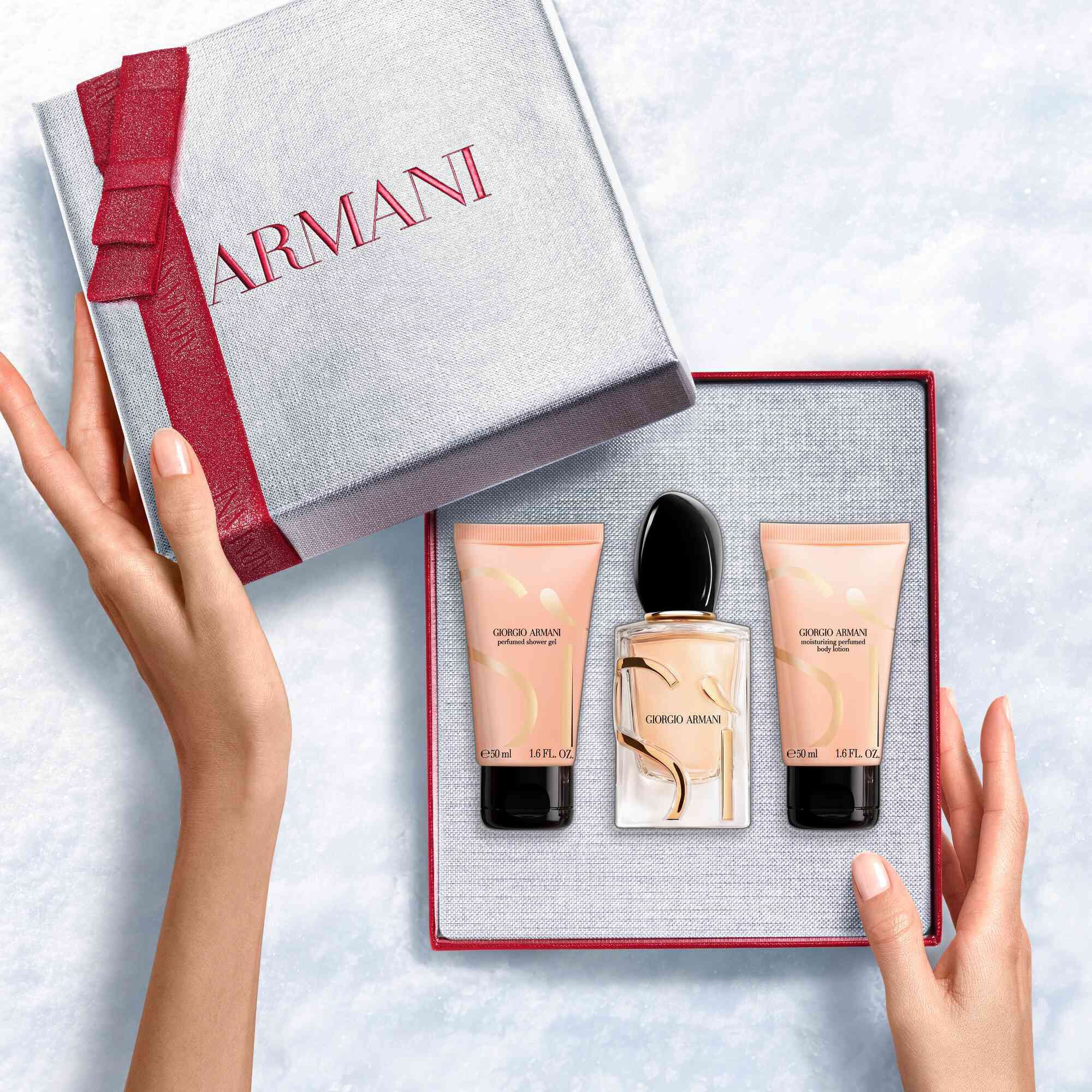 Hands unveiling a red-ribboned white Armani gift box with Si Eau de Parfum 50ml, 50ml perfumed body lotion and 50ml perfumed shower gel— a refined women's floral fragrance gift set.