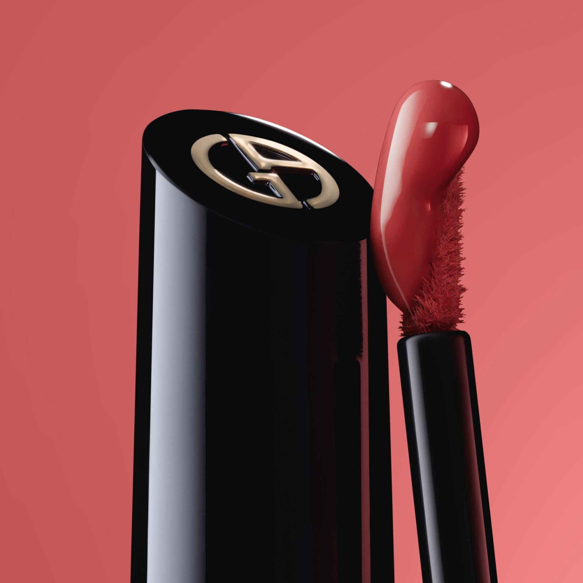 Close-up of the black ARMANI LIP MAESTRO cap with gold logo and its applicator coated in shade 520 Dusty Rose against a pink background.