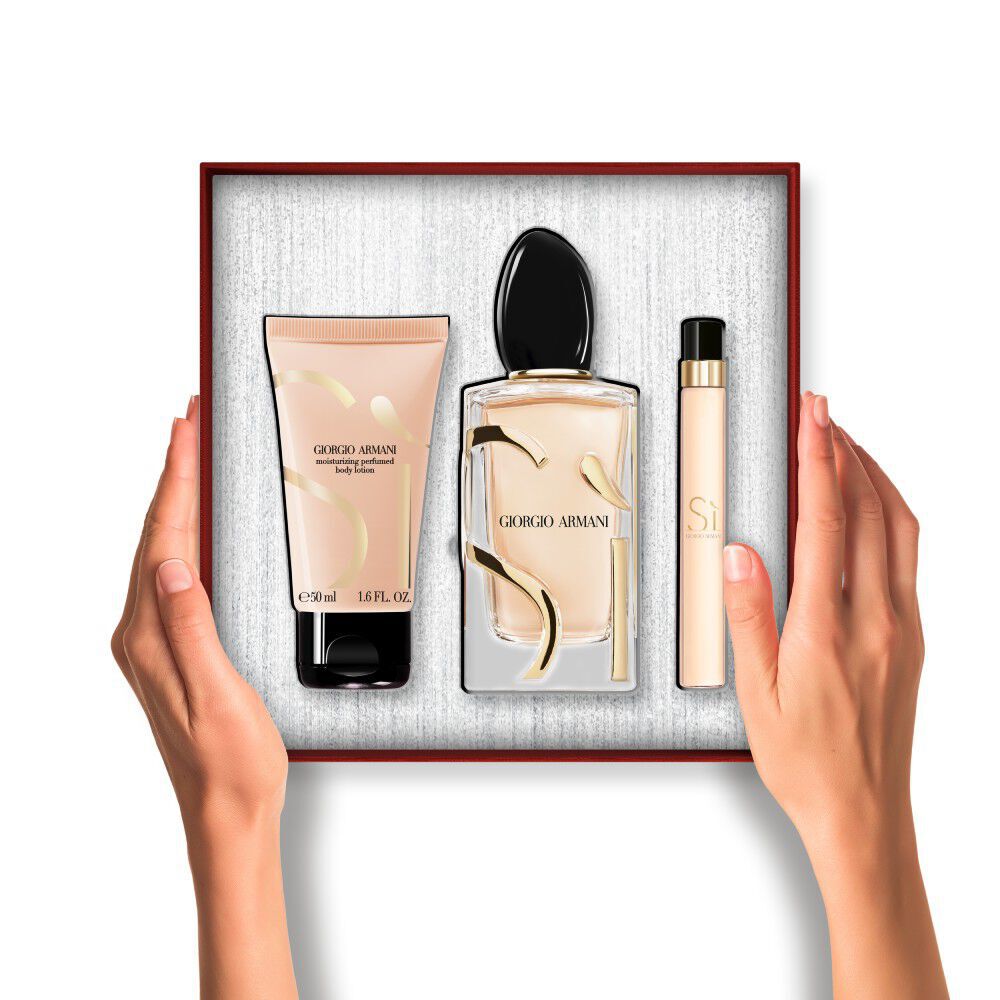 Hands holding an Armani Si Eau de Parfum perfume, travel spray and Bodey lotion set inside a gift box.	