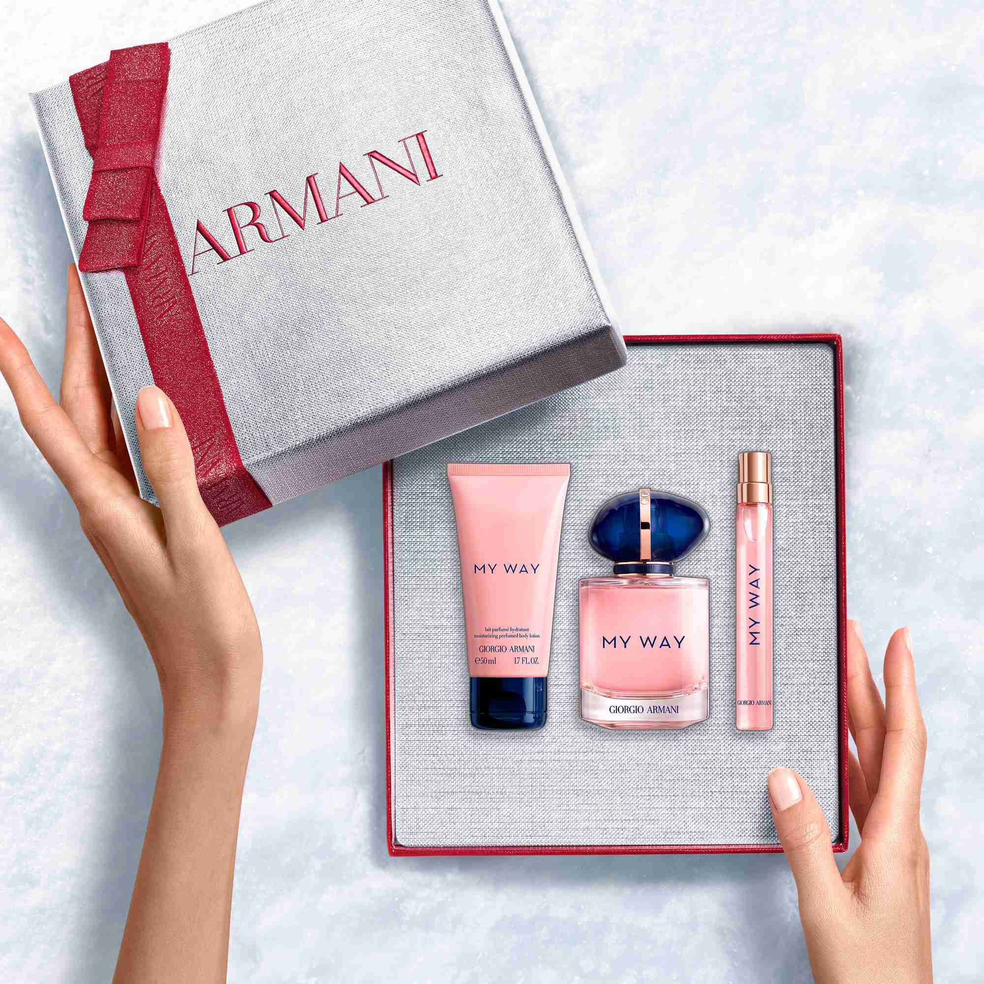 Hands unveiling a ruby-ribboned white Armani gift box with My My Way Eau de Parfum 90ml fragrance, 10ml bottle and 50ml perfumed body lotion— a refined women's floral fragrance gift set.