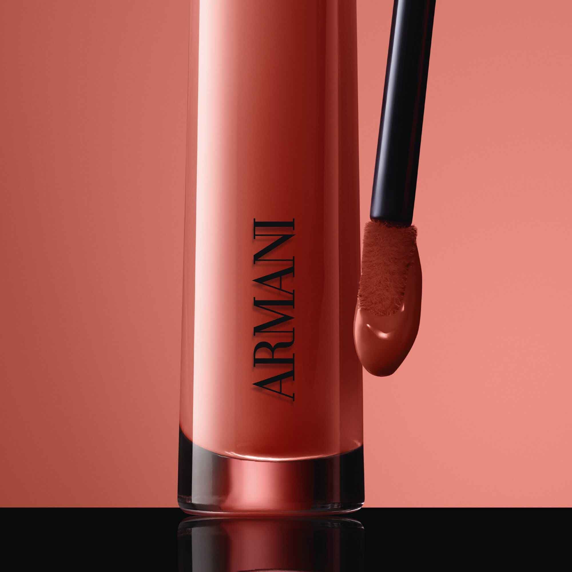 Close-up of the black ARMANI LIP MAESTRO cap with gold logo and its applicator coated in shade 520 Dusty Rose against a pink background.