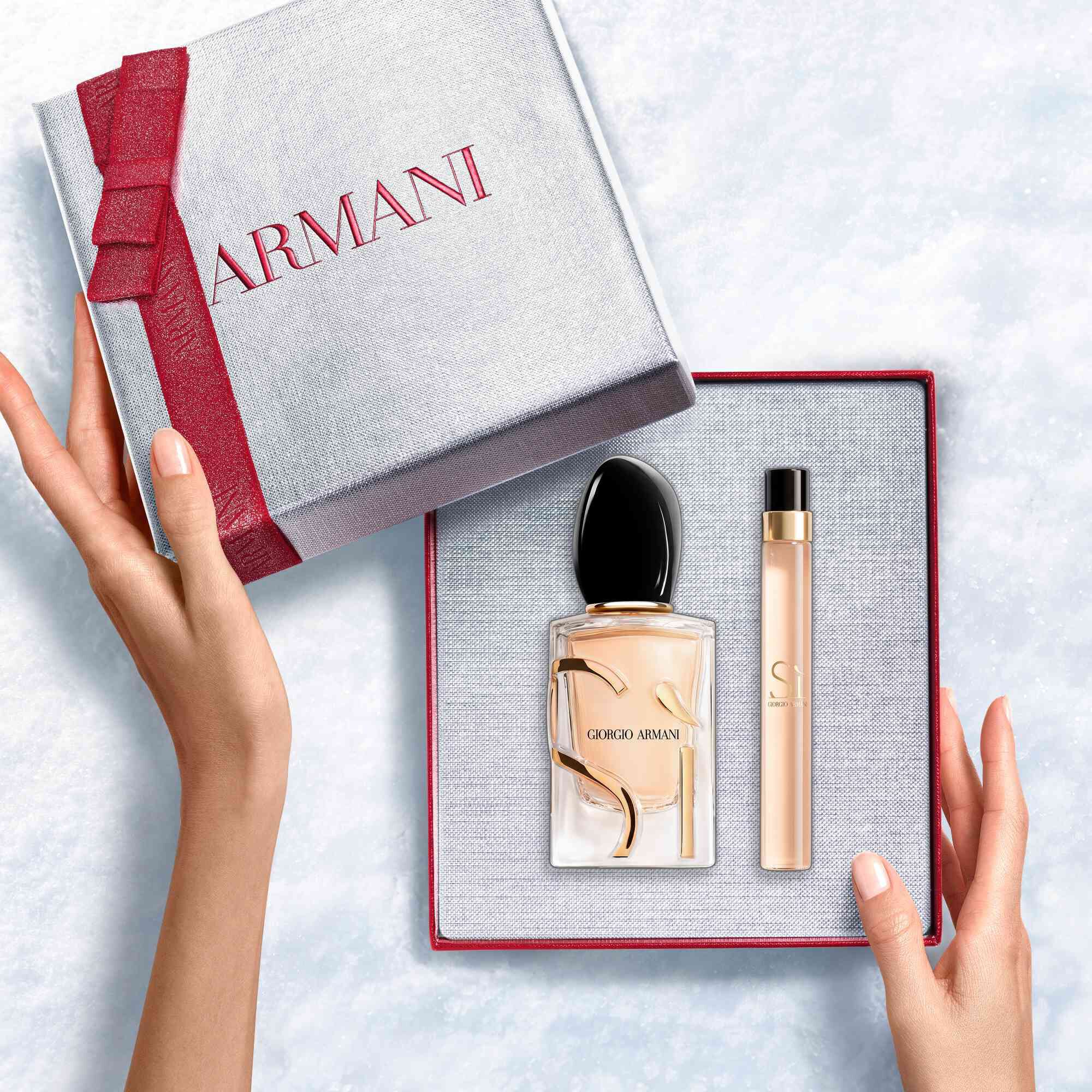 Hands unveiling a red-ribboned white Armani gift box with Si Eau de Parfum 50ml and 10ml — a refined women's floral fragrance gift set.