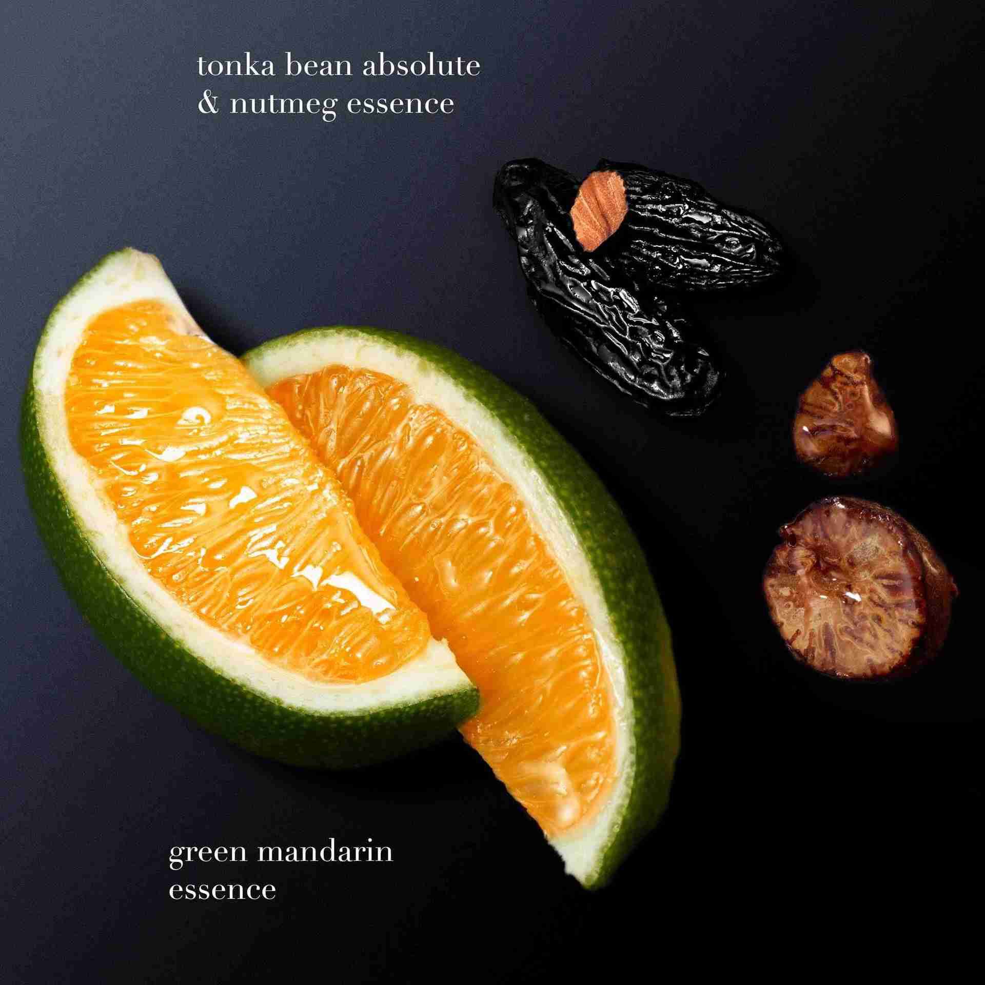 A slice of green mandarin and pieces of tonka bean with cut citrus, labeled as "green mandarin essence" and "tonka bean absolute & cutting essence," arranged on a dark background.