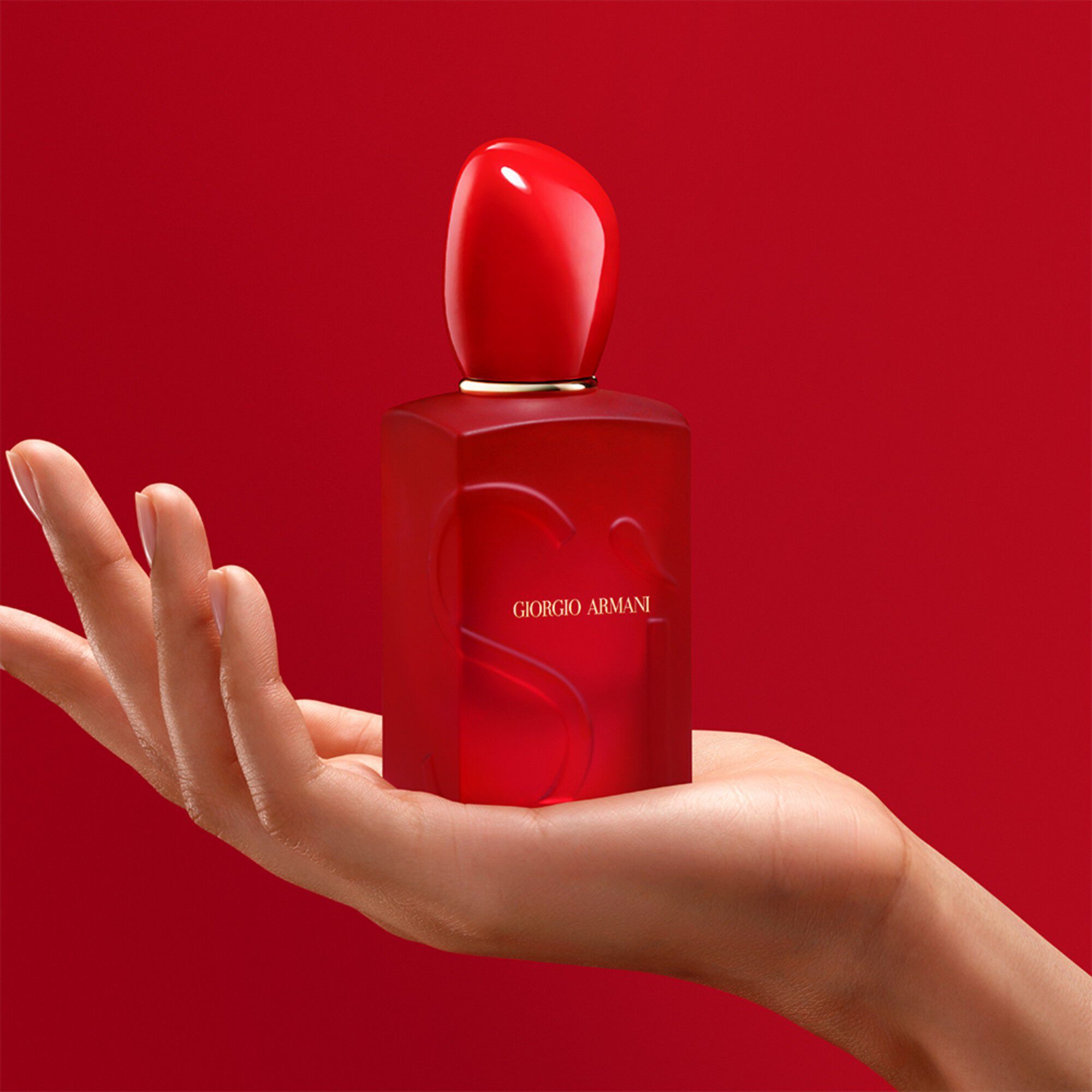 Hand holding the Giorgio Armani Si Passione Red Bloom bottle on a red background.