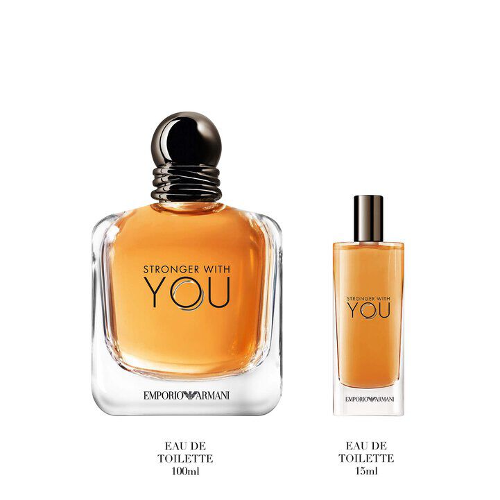 Two bottles of Armani STRONGER WITH YOU EAU DE TOILETTE shown on a textured blue surface, emphasizing the bold amber color and luxurious design of the fragrance.