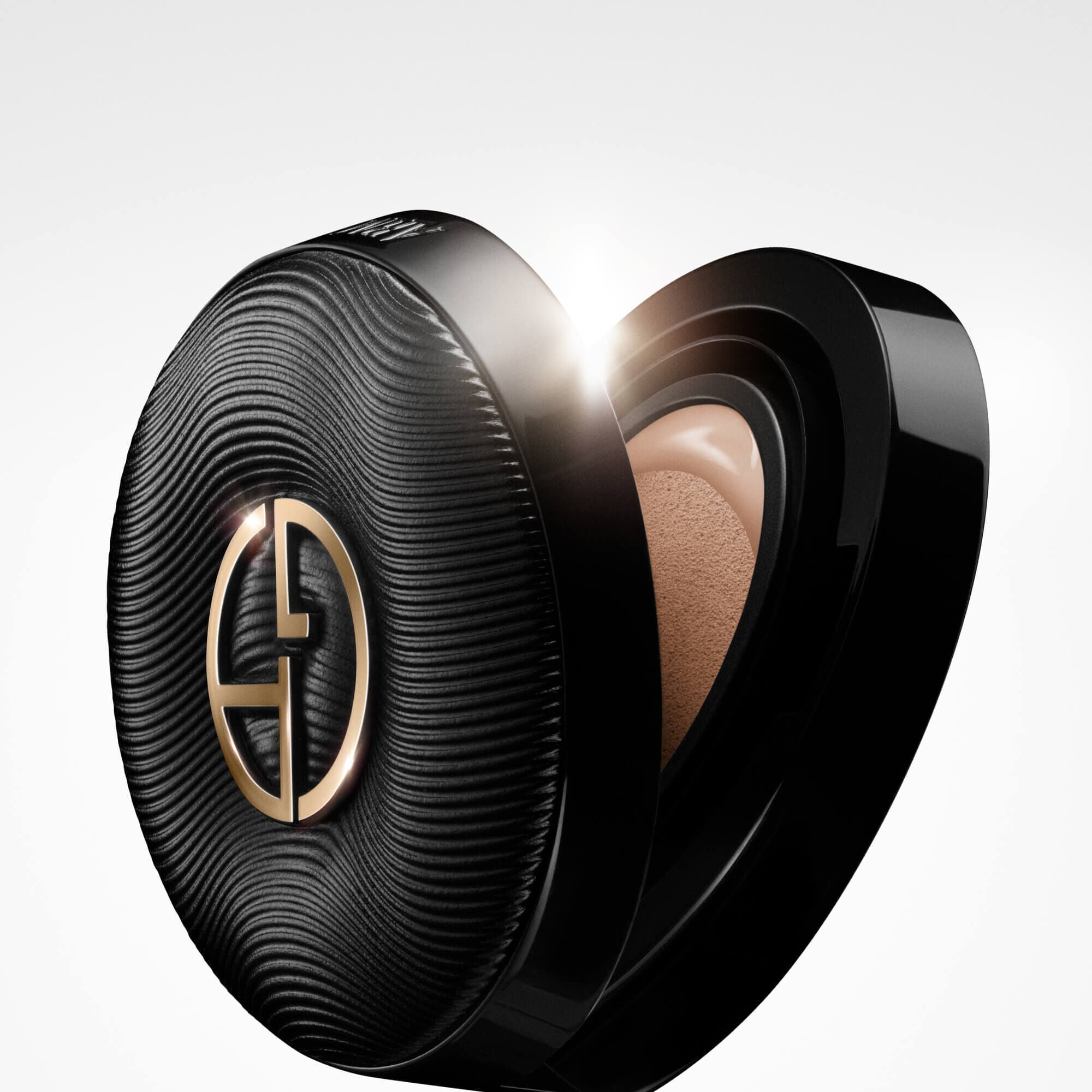 A sleek, black Giorgio Armani LUMINOUS SILK PRIMA GLOW CUSHION compact partially open, revealing the foundation cushion inside, with a bright lens flare highlighting its luxurious design.