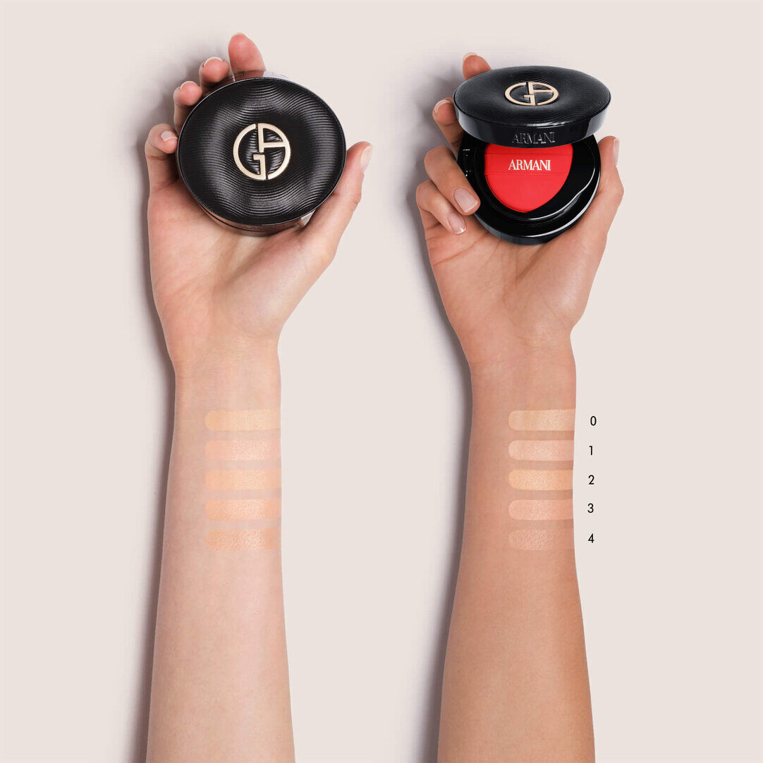 Two hands holding Giorgio Armani LUMINOUS SILK PRISMA GLOW CUSHION compacts, with foundation swatches labeled 0 through 4 on the forearms to display different shades