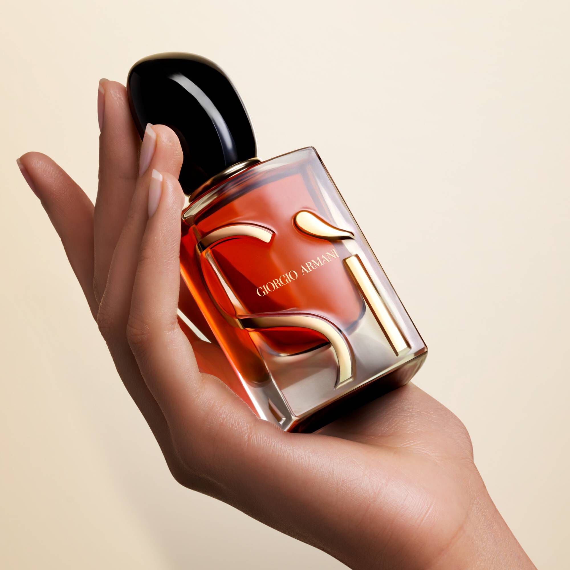 A hand gracefully holds a Giorgio Armani Si perfume bottle against a soft, neutral background.
