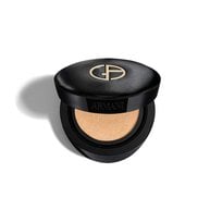 An open Giorgio Armani LUMINOUS SILK PRIMA GLOW CUSHION compact. The sleek black case features a textured lid with a prominent golden GA logo. Inside, a light beige liquid foundation is visible, absorbed within a soft sponge cushion.