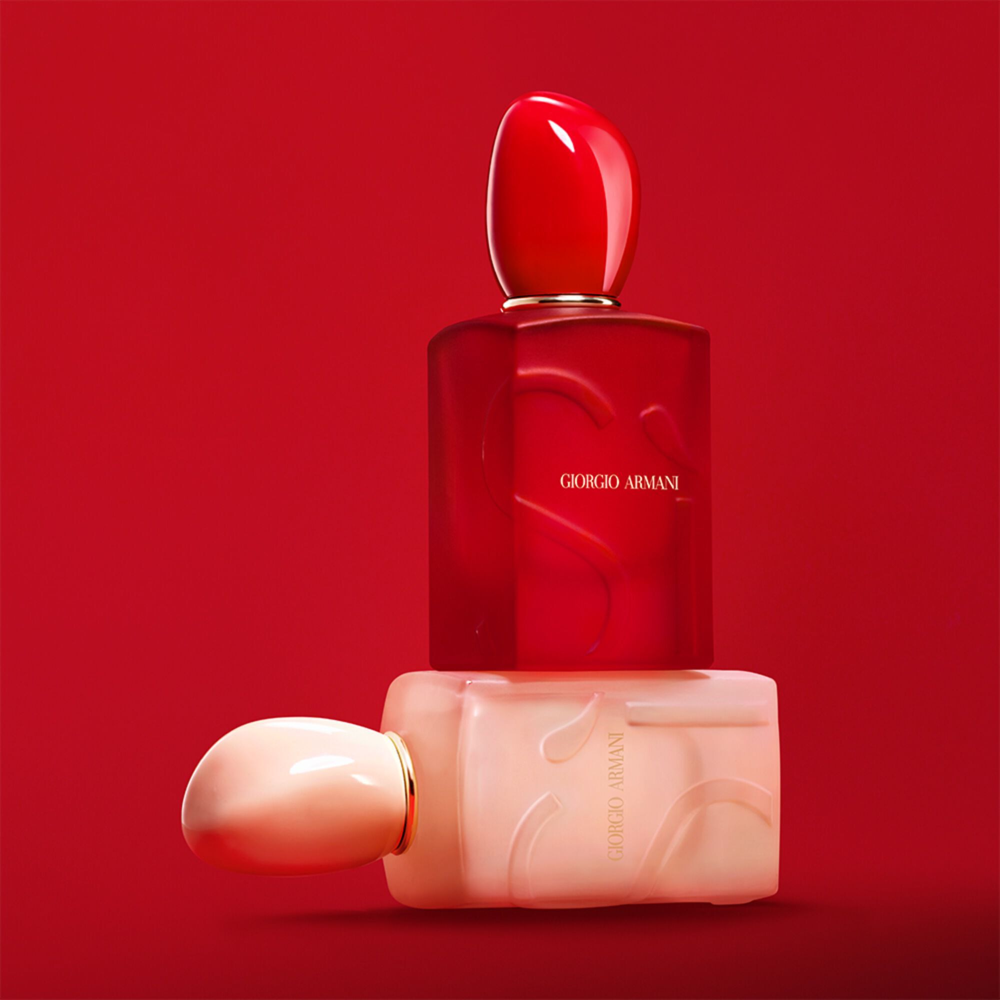 Giorgio Armani Si Nude Bloom and Si Passione Red Bloom bottles stacked on a red background.