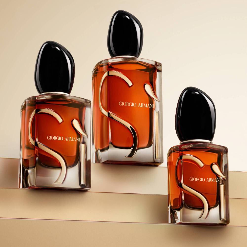 Three Giorgio Armani Si perfume bottles of varying heights, arranged on stepped, neutral-toned surfaces, highlighting their amber liquid and distinctive 'Si' design.
